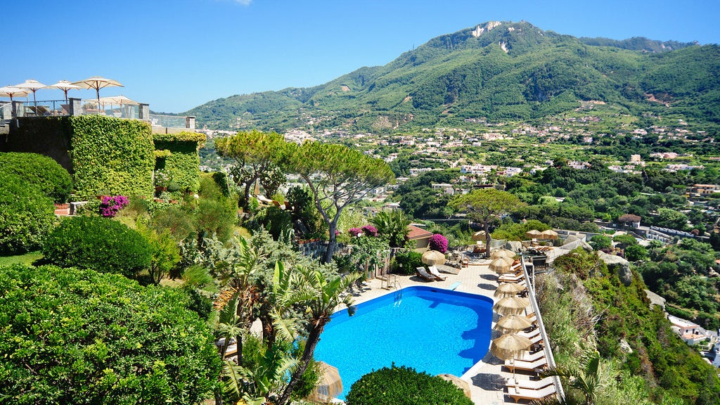 Mediterranean luxury resort perched on hilltop overlooking Ischia coastline, featuring infinity pool merging with blue sea horizon