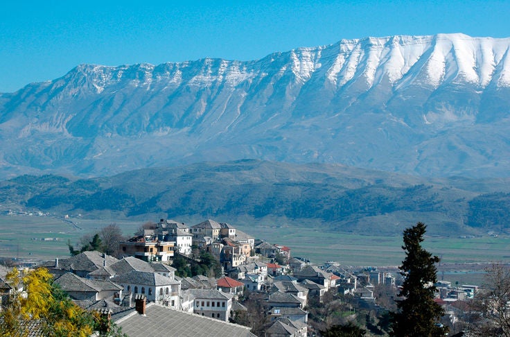 Pristine turquoise Blue Eye Spring in southern Albania, surrounded by lush greenery with elegant travelers enjoying gourmet local cuisine on a scenic outdoor terrace