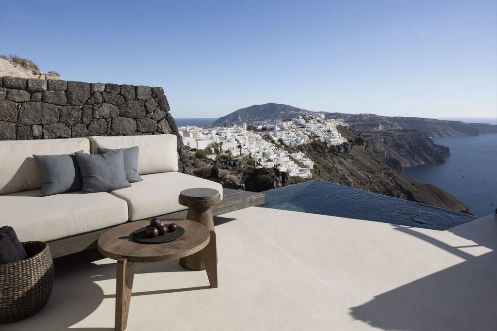 Luxurious white cave villa with infinity pool perched on Santorini cliffs, overlooking the Aegean Sea's blue waters at sunset