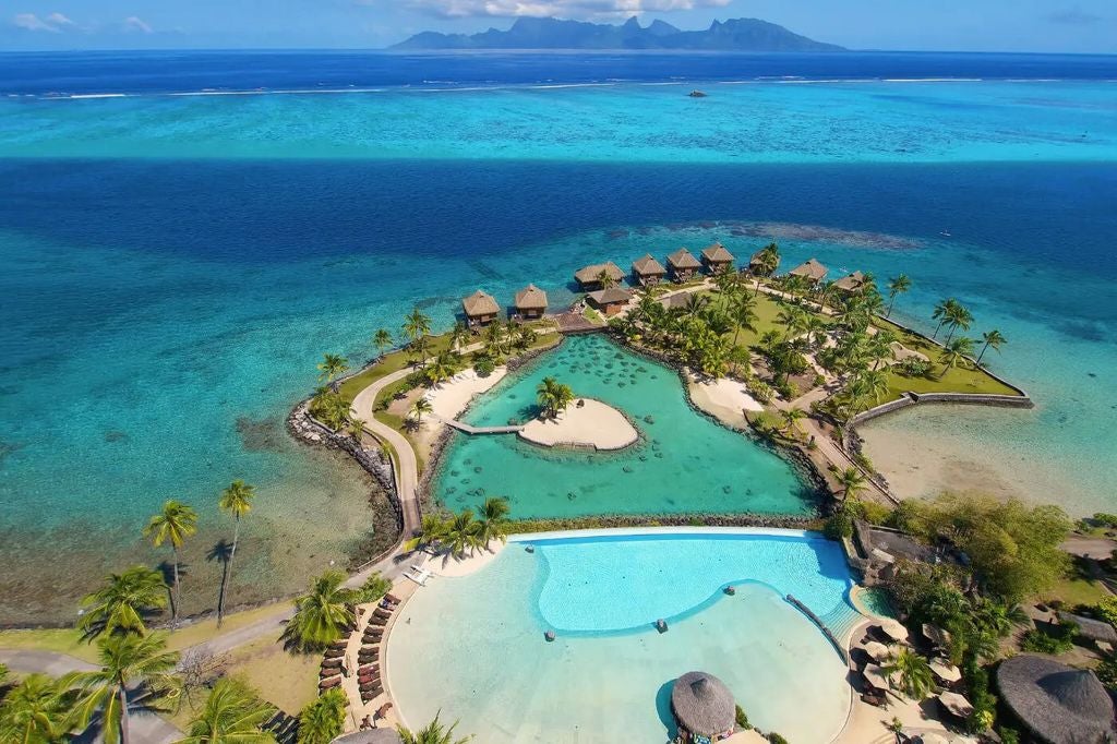 Luxurious overwater bungalows at Intercontinental Tahiti resort stretch across turquoise lagoon waters against lush mountain backdrop