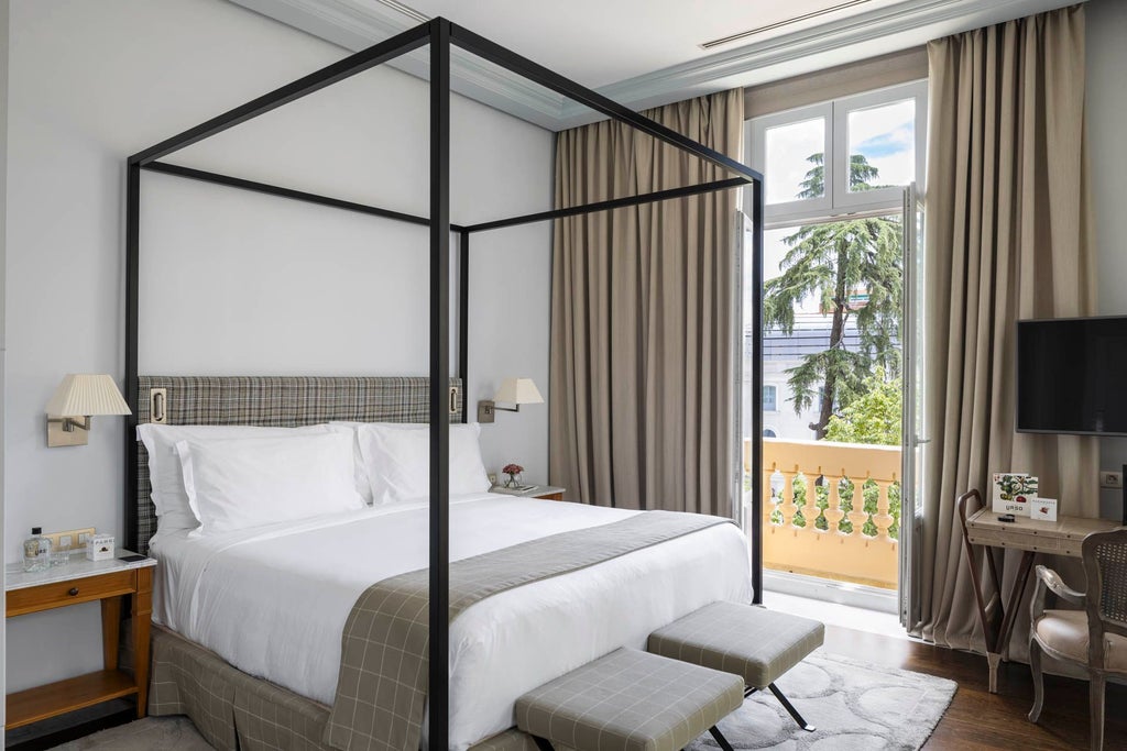 Elegant junior suite with plush white bed, ornate headboard, large windows overlooking Madrid's historic palace, warm neutral tones, and luxurious spa-like design