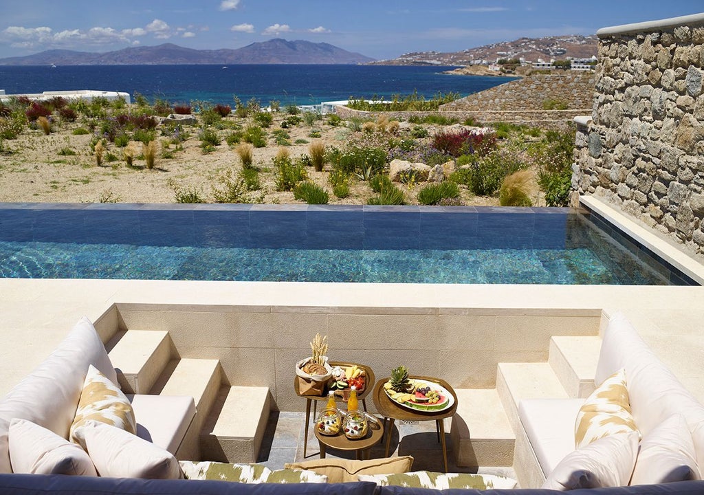 Luxurious one-bedroom villa in Mykonos with private heated pool, overlooking azure Aegean Sea, featuring modern Greek island design and panoramic coastal views