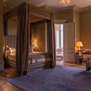 Elegant French château hotel bedroom with ornate chandelier, antique furnishings, soft cream walls, and delicate period decor reflecting refined 18th-century style