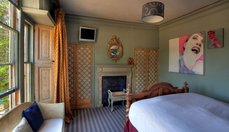 Elegantly styled Venetian-inspired hotel room at Strattons Hotel with rich fabric textures, antique furnishings, and warm ambient lighting in soft neutral tones.