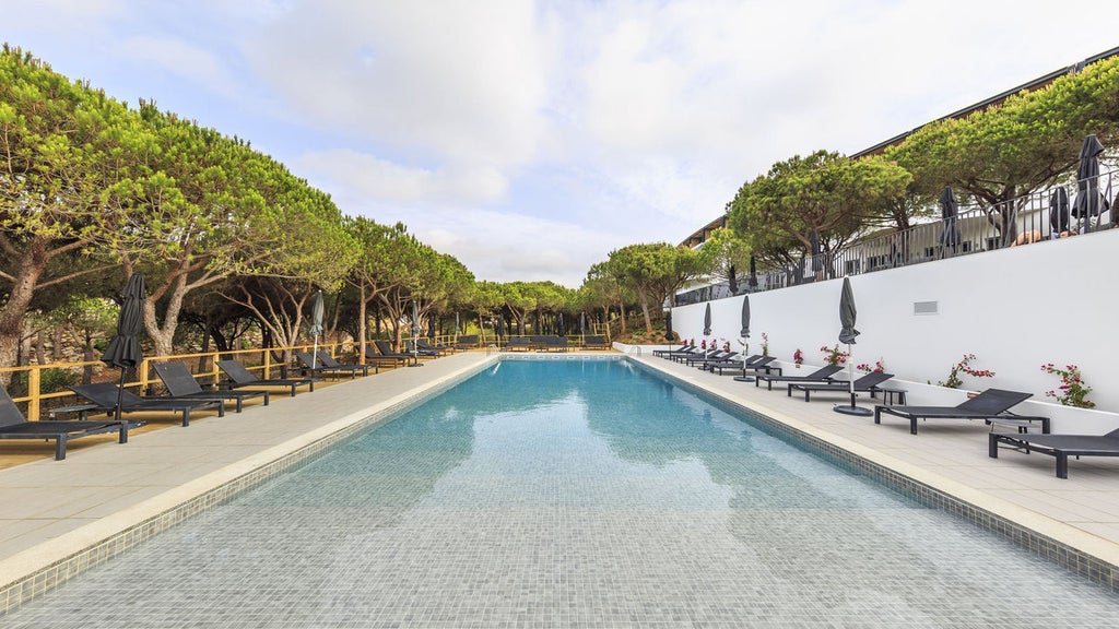 White modern luxury resort with floor-to-ceiling windows nestled among pine trees, overlooking the pristine beach of Praia Verde, Portugal