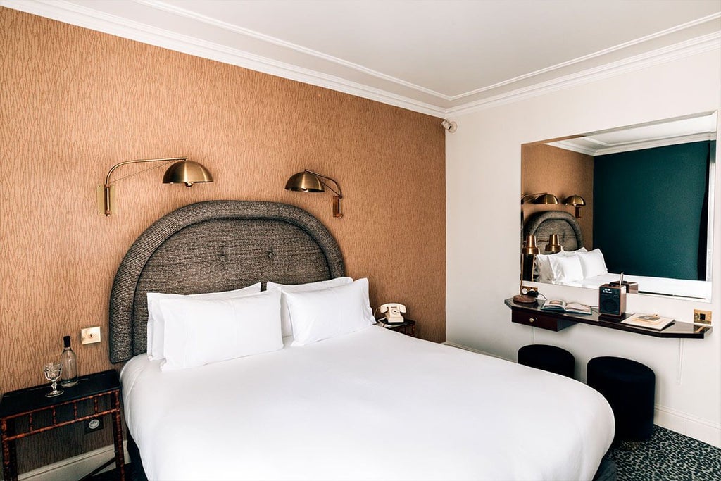 Elegant Parisian hotel room with plush burgundy bedding, herringbone wood floors, and chic retro-modern decor in warm neutral tones