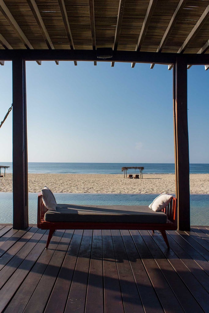 Minimalist beachfront hotel with white-washed walls, thatched roof, and infinity pool overlooking Pacific Ocean waves in scenic Mexican coastal landscape