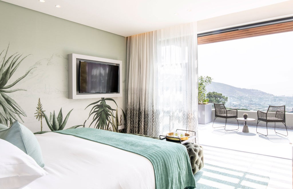 Modern boutique hotel suite with elegant white decor, floor-to-ceiling windows overlooking Table Mountain, and freestanding soaking tub