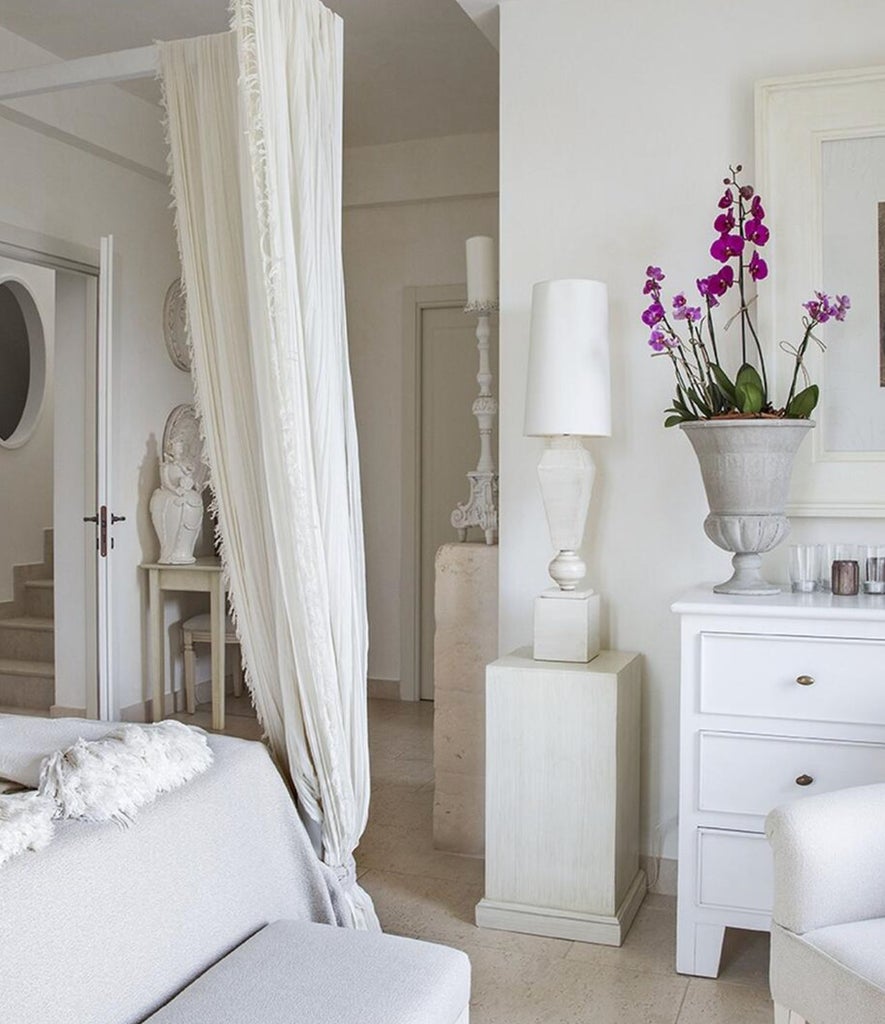 Elegant Italian hotel suite with vaulted stone ceiling, rustic white walls, king bed with crisp linens, and romantic ambient lighting