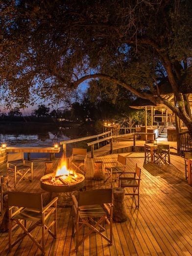 Luxurious safari tented camp nestled in lush Botswana wilderness, with raised wooden walkways, contemporary design, and dramatic landscape beyond.