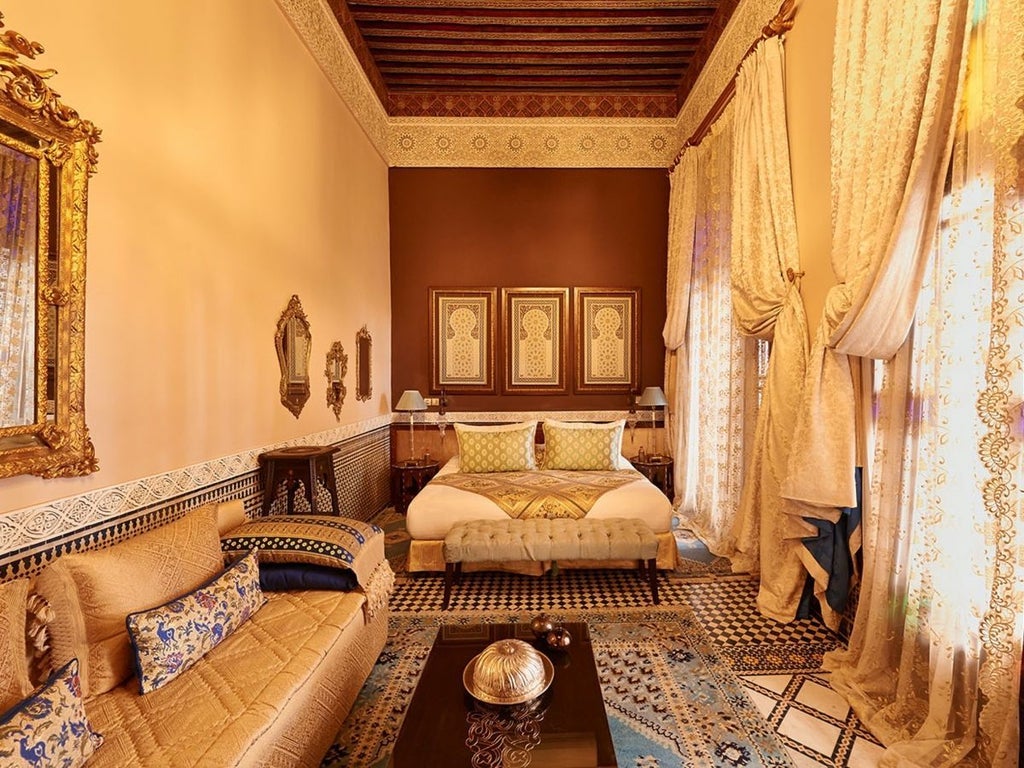 Elegant Moroccan riad superior deluxe room with intricate zellige tilework, ornate chandelier, plush bedding, and traditional arabesque architectural details