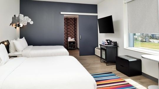 Modern hotel room with two plush queen beds, sleek contemporary design, crisp white linens, and stylish urban decor at Scenset Charlotte Airport location