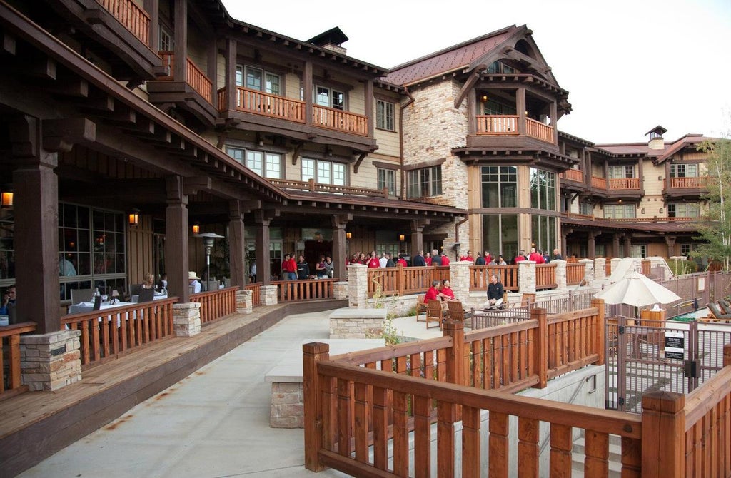 Luxurious mountain resort with stone facade, snow-covered peaks backdrop, grand entrance with timber beams and outdoor fire pits