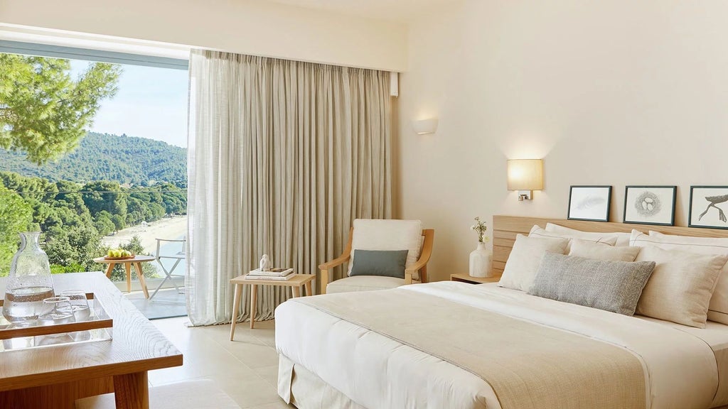 Luxurious double room at ELIVI Skiathos with elegant white decor, wooden furnishings, and a private balcony overlooking lush Greek island scenery.