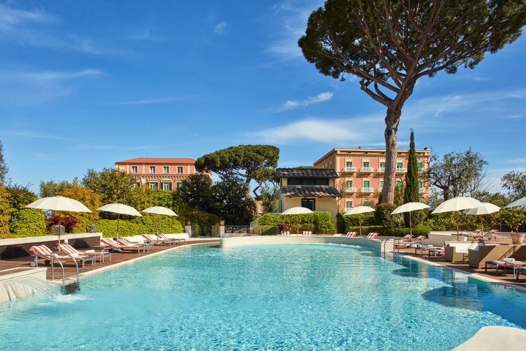 Elegant five-star Italian hotel with neoclassical facade, grand entrance with marble columns, and lush Mediterranean gardens overlooking the sea