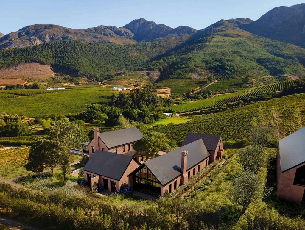 Luxurious boutique hotel nestled in lush South African landscape, featuring elegant white architecture with vibrant green gardens and mountain backdrop