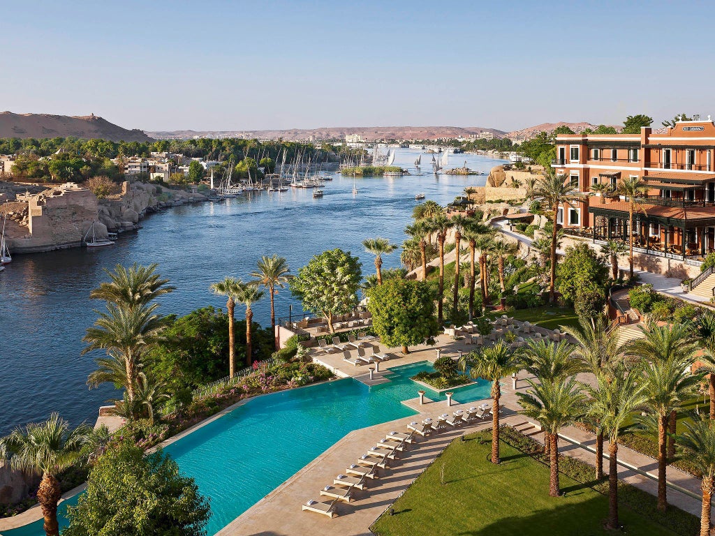 Elegant Sofitel Legend hotel overlooking the Nile, with colonial-style architecture, lush gardens, and golden sunset reflecting on historic Aswan landscape