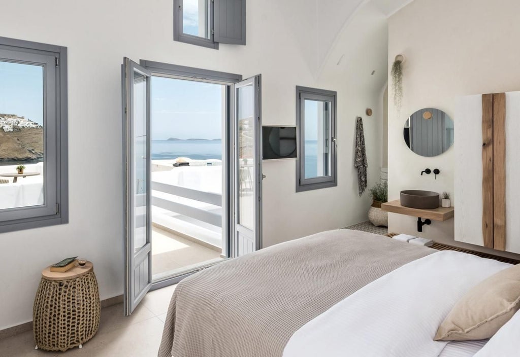 Elegant Santorini-style honeymoon suite with white-washed walls, minimalist decor, private balcony overlooking azure Aegean Sea, soft sunlight filtering through sheer curtains