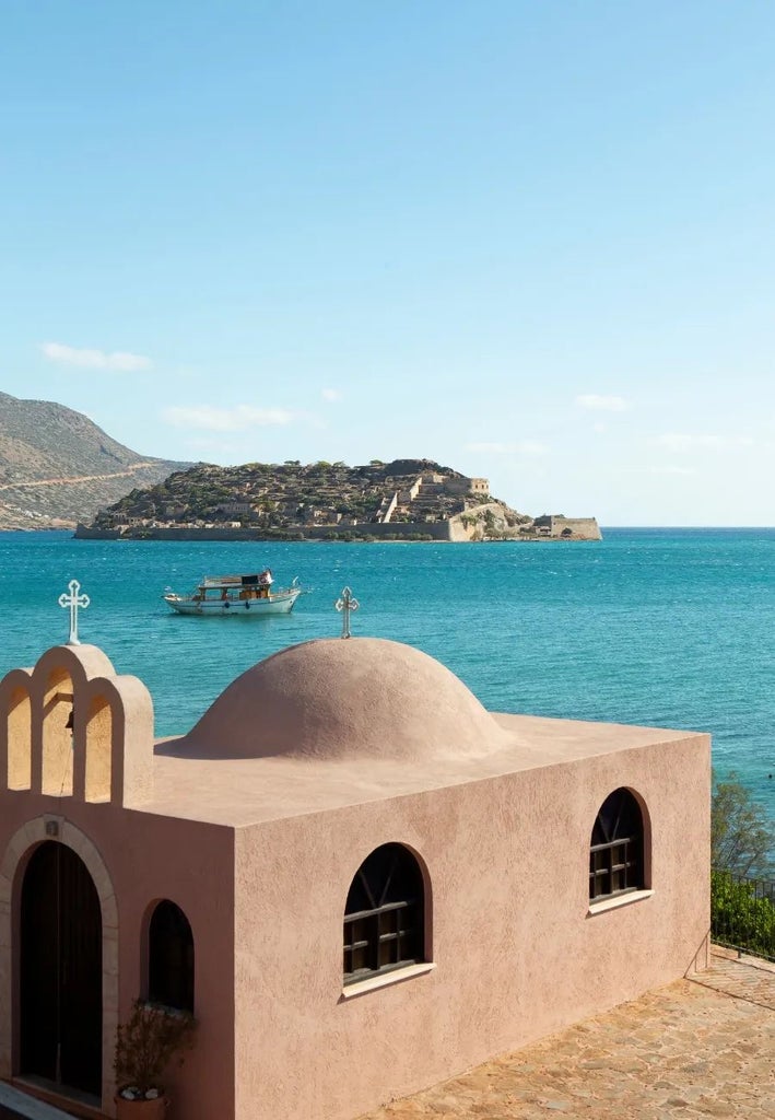 Luxurious beachfront resort with white domed architecture, azure Aegean waters, and elegant infinity pool overlooking scenic Cretan coastline at sunset