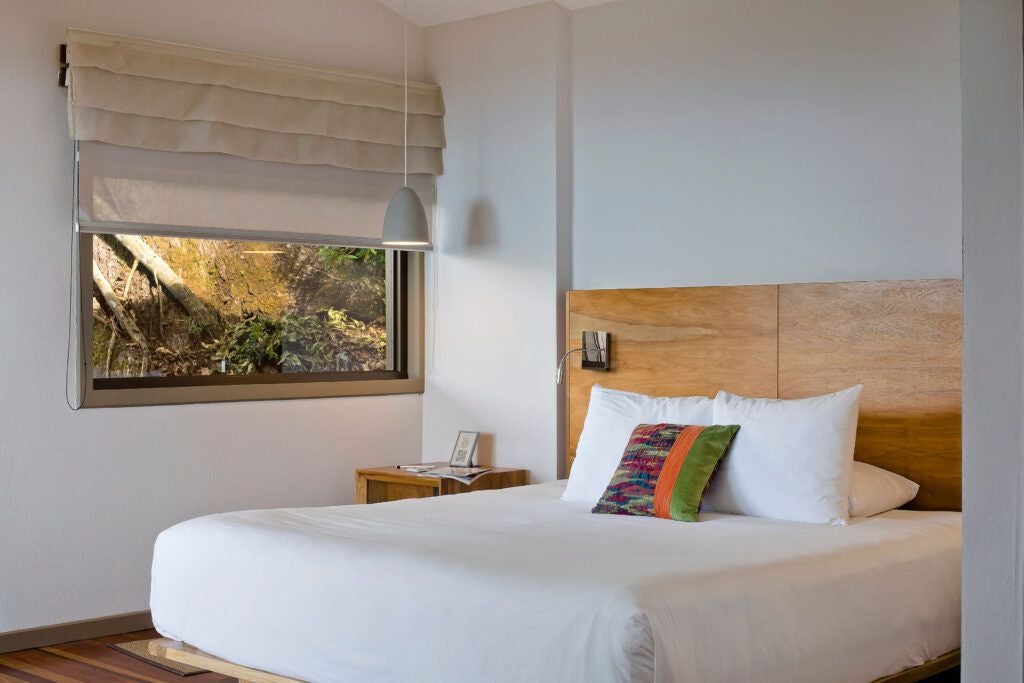 Elegant wooden-paneled suite with floor-to-ceiling windows, revealing lush Costa Rican rainforest, modern minimalist decor, and natural light streaming in