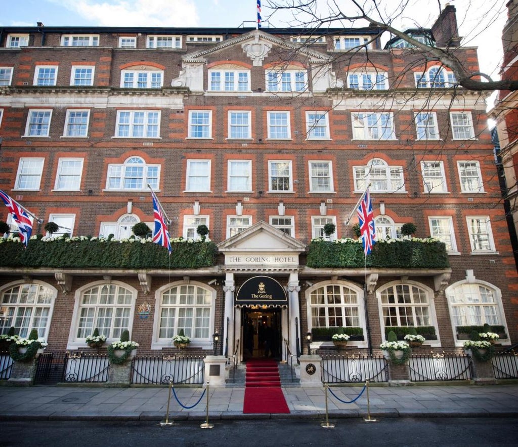 Elegant white facade of The Goring London hotel with Union Jack flags, featuring ornate Victorian architecture and manicured topiary plants