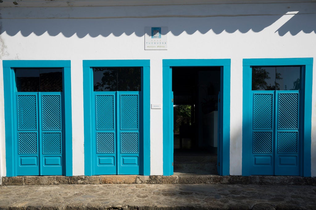 Luxurious turquoise boutique hotel facade in Paraty, Brazil, with colonial-style white architecture and vibrant tropical landscaping at sunset