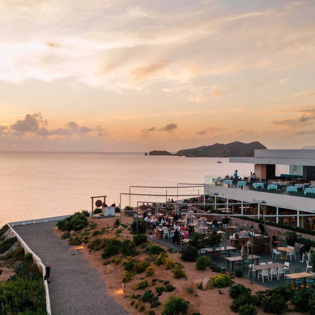 Luxurious white cliff-side resort overlooking azure Mediterranean waters, featuring sleek infinity pool and modern architectural design in Ibiza, Spain