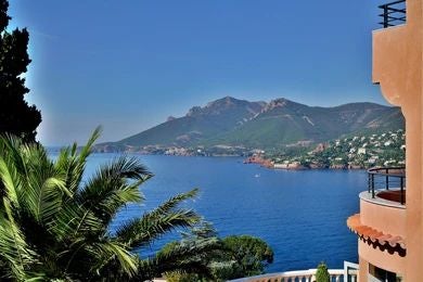 Luxurious seaside hotel with white façade nestled on French Riviera cliff, overlooking azure Mediterranean waters and lush coastal landscape