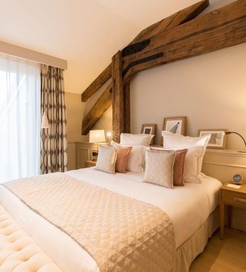 Elegant deluxe hotel room with soft neutral tones, plush bedding, modern furnishings, and large windows overlooking scenic French architecture at Chais Monnet & Spa