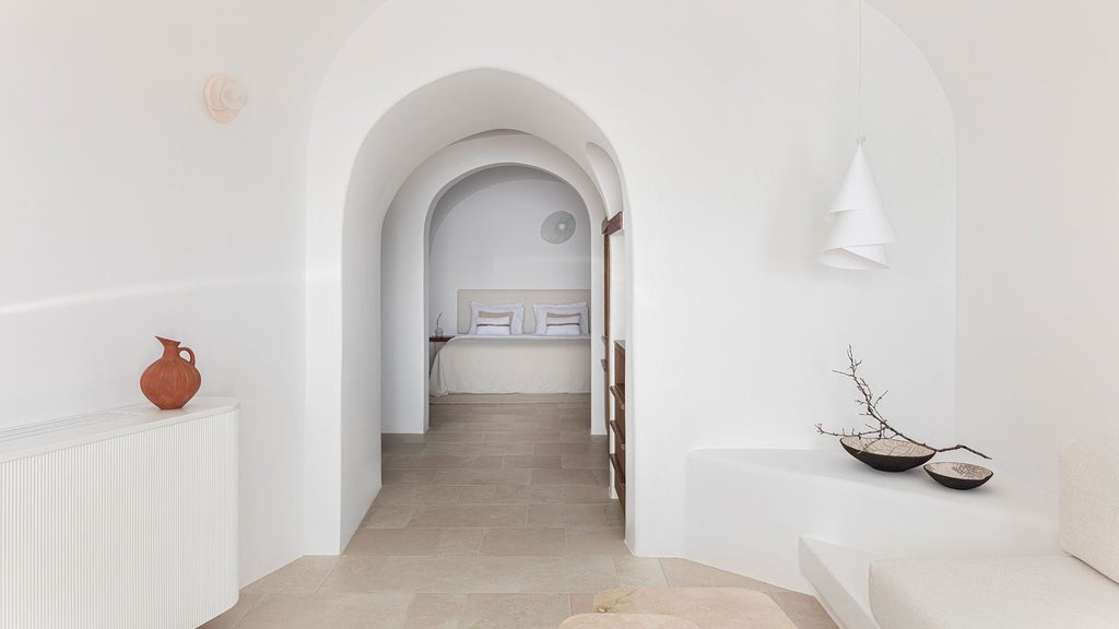 Luxurious Santorini suite with minimalist white decor, panoramic sea view, private balcony, and elegant modern furnishings overlooking the azure Aegean waters