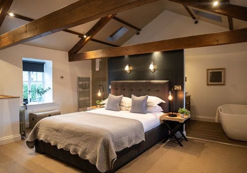 Spacious luxury barn suite with plush king bed, contemporary stone walls, and elegant wooden furnishings at a charming UK countryside boutique hotel.