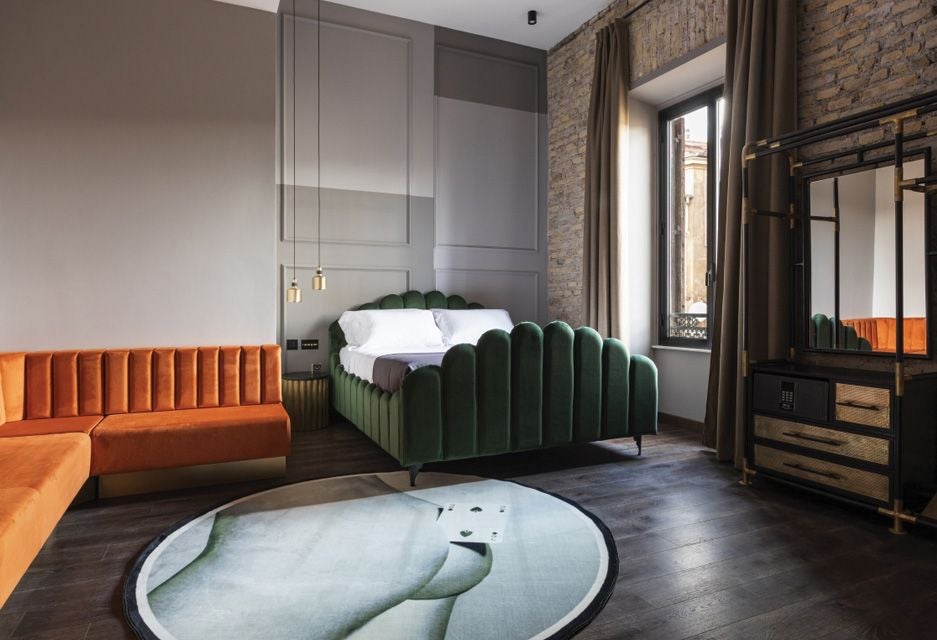 Elegant loft-style hotel room in Rome with minimalist design, high ceilings, hardwood floors, and contemporary Italian furnishings bathed in warm natural light