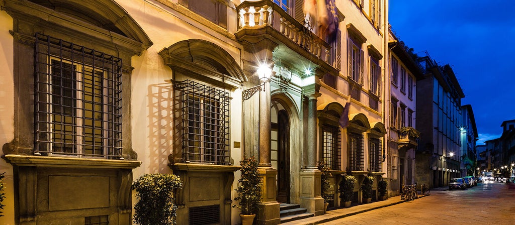 Elegant Florentine hotel room with crystal chandelier, ornate ceiling frescoes, period furniture and tall windows with city views