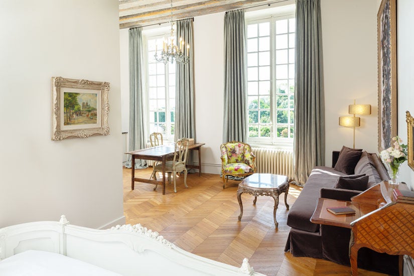 Opulent French château hotel studio with ornate period furniture, crystal chandelier, herringbone floors and garden-view windows