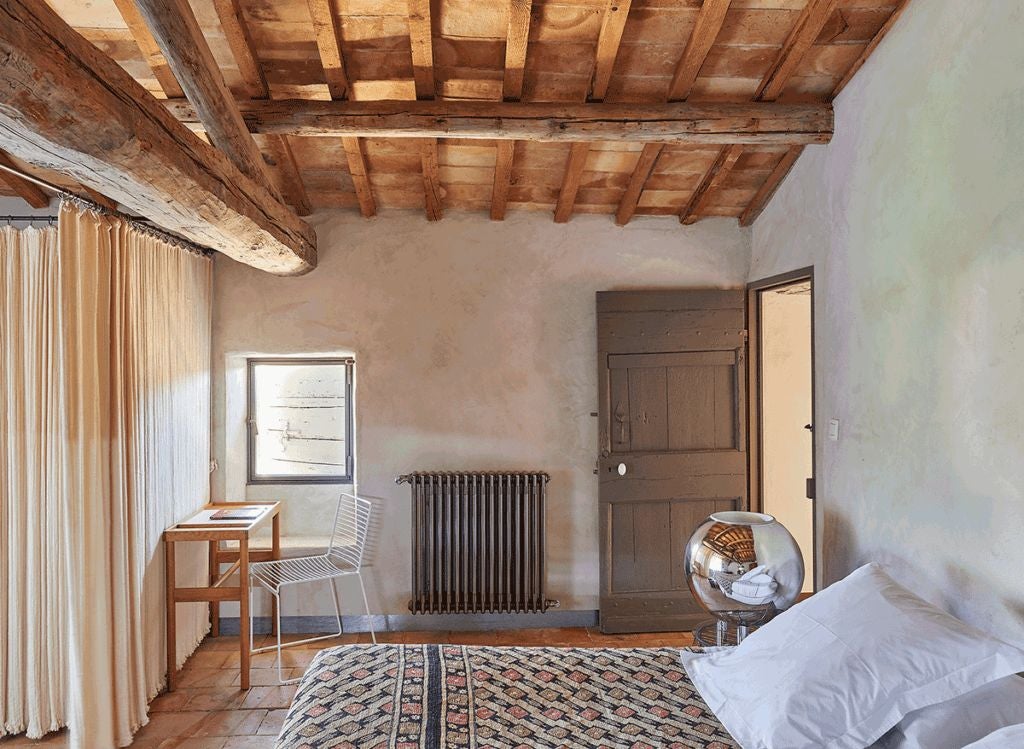 Elegant stone-walled bedroom with rustic wooden furniture, soft linens, and large windows overlooking lavender fields in Provence, France