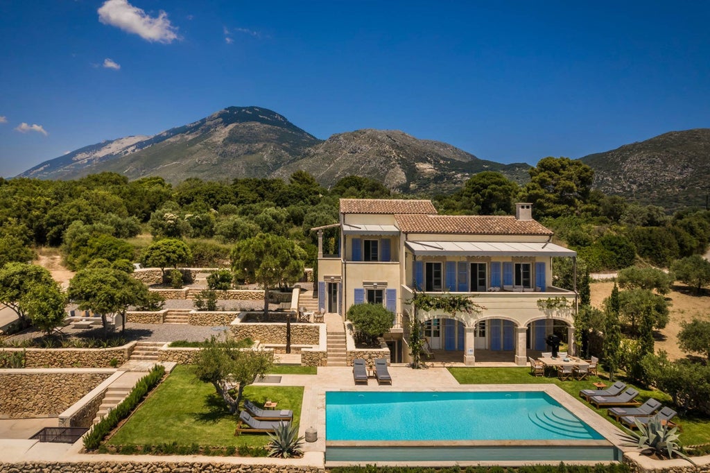 Elegant stone villa with terracotta roof overlooking azure Aegean Sea, surrounded by lush Mediterranean gardens and rustic stone walls