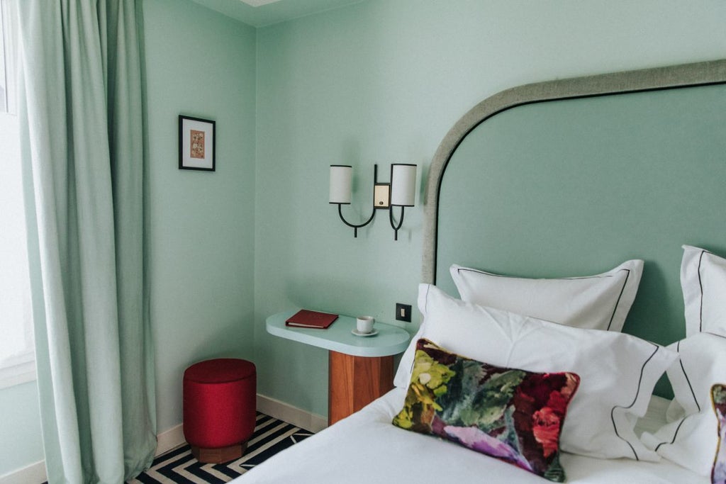 Elegant Parisian-style double room with soft pastel wallpaper, vintage wooden furniture, ornate bed linens, and warm ambient lighting at Hôtel Bienvenue