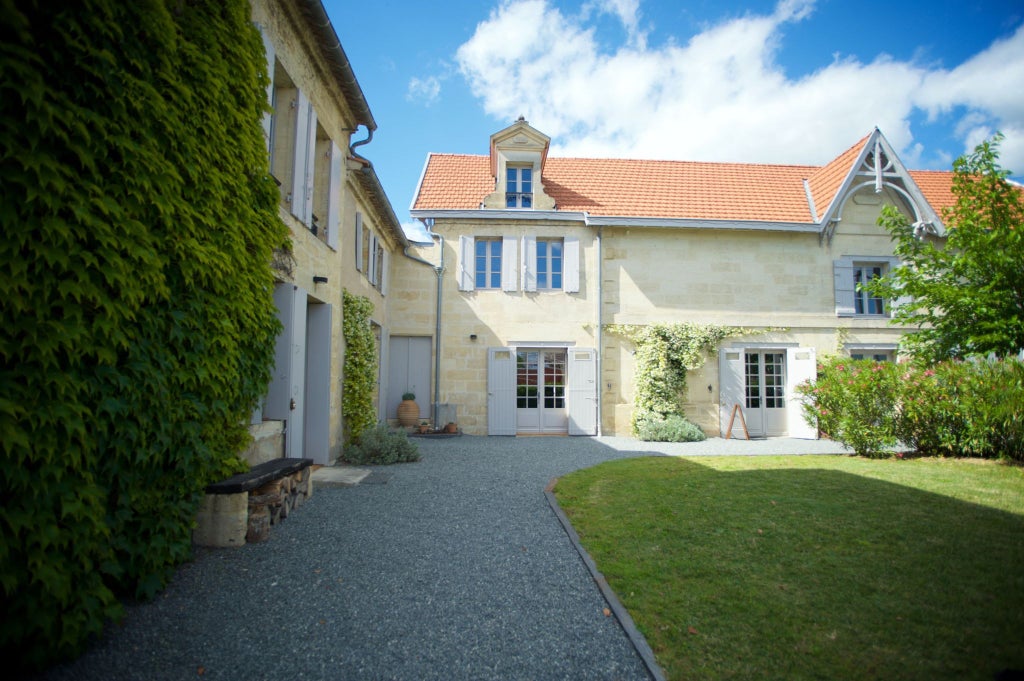 Elegant French countryside hotel with stone facade, lush gardens, and classic architecture nestled in verdant Burgundy wine region landscape at dusk