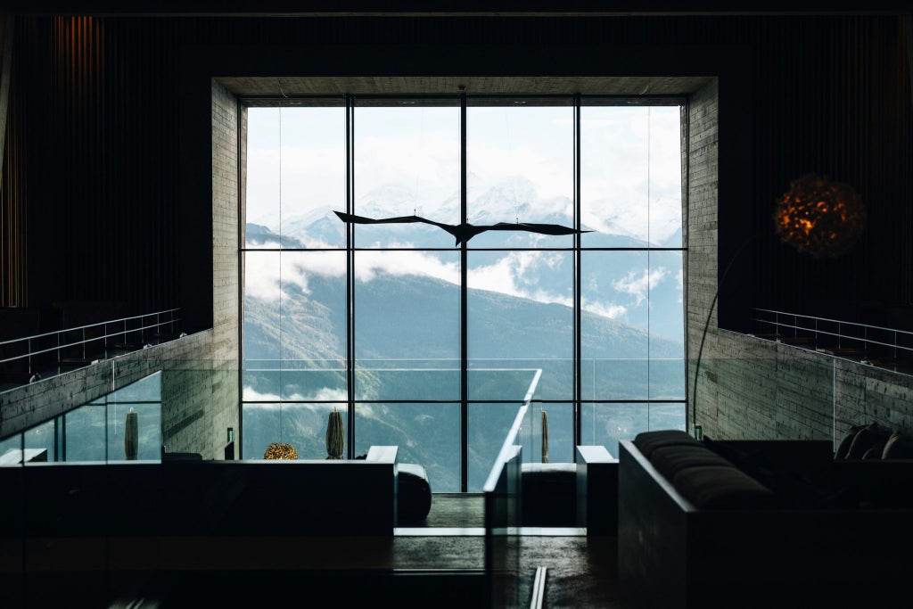 Luxurious alpine hotel Chetzeron perched on rocky mountainside with panoramic Swiss Alps view, modern minimalist architecture blending with rugged landscape