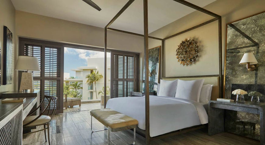 Elegant resort room with king bed, floor-to-ceiling windows overlooking ocean, modern decor, marble bathroom and private balcony