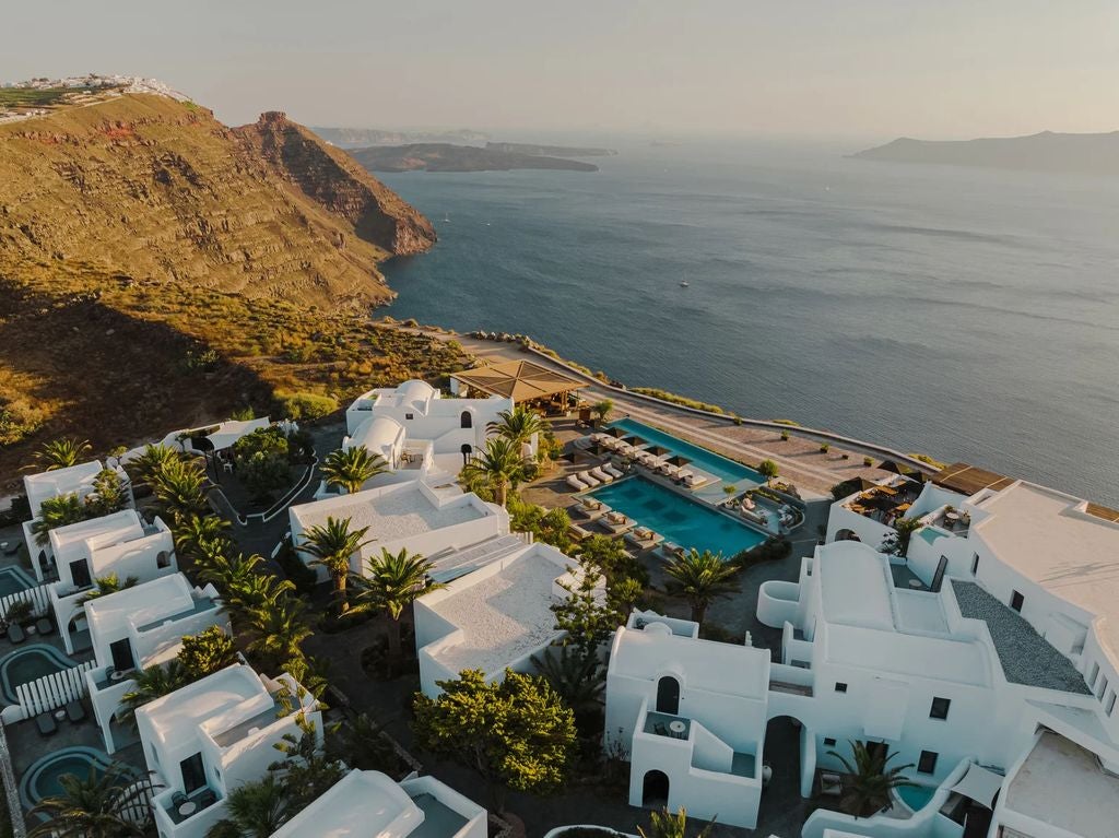 Luxurious infinity pool overlooking Santorini's caldera at sunset, with white minimalist loungers and volcanic cliffside architecture