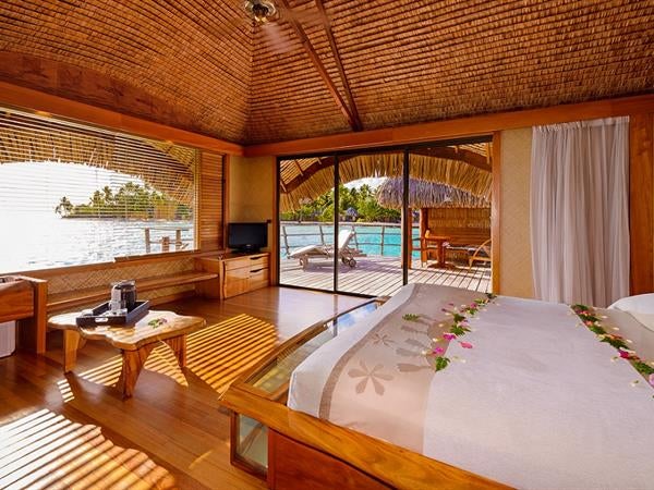 Luxurious overwater bungalow suite with private deck, glass floor panels, and panoramic views of turquoise lagoon at sunset in Tahaa