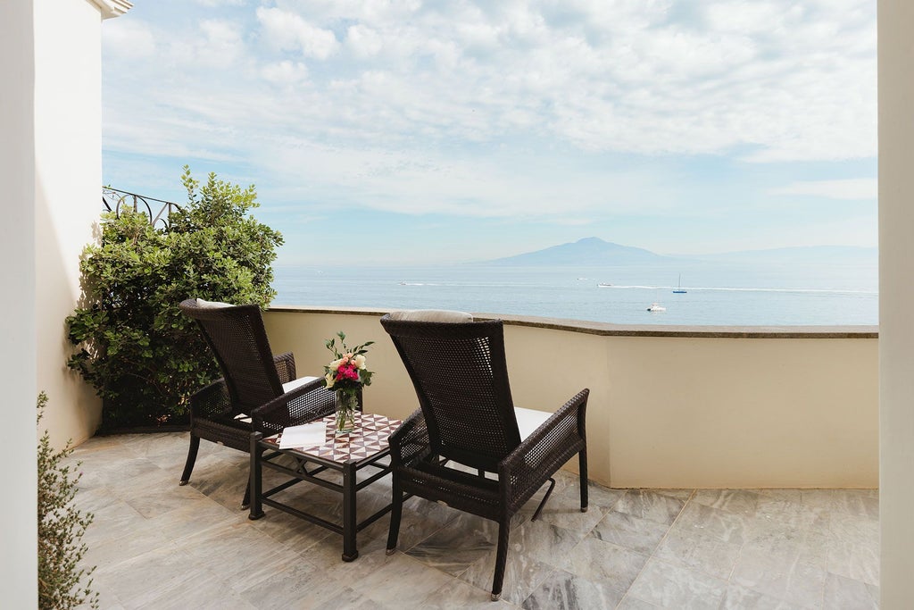 Luxurious coral-toned suite with panoramic Mediterranean view, elegant maritime-inspired decor, and stunning Sorrento coastline backdrop from Bellevue Syrene Hotel