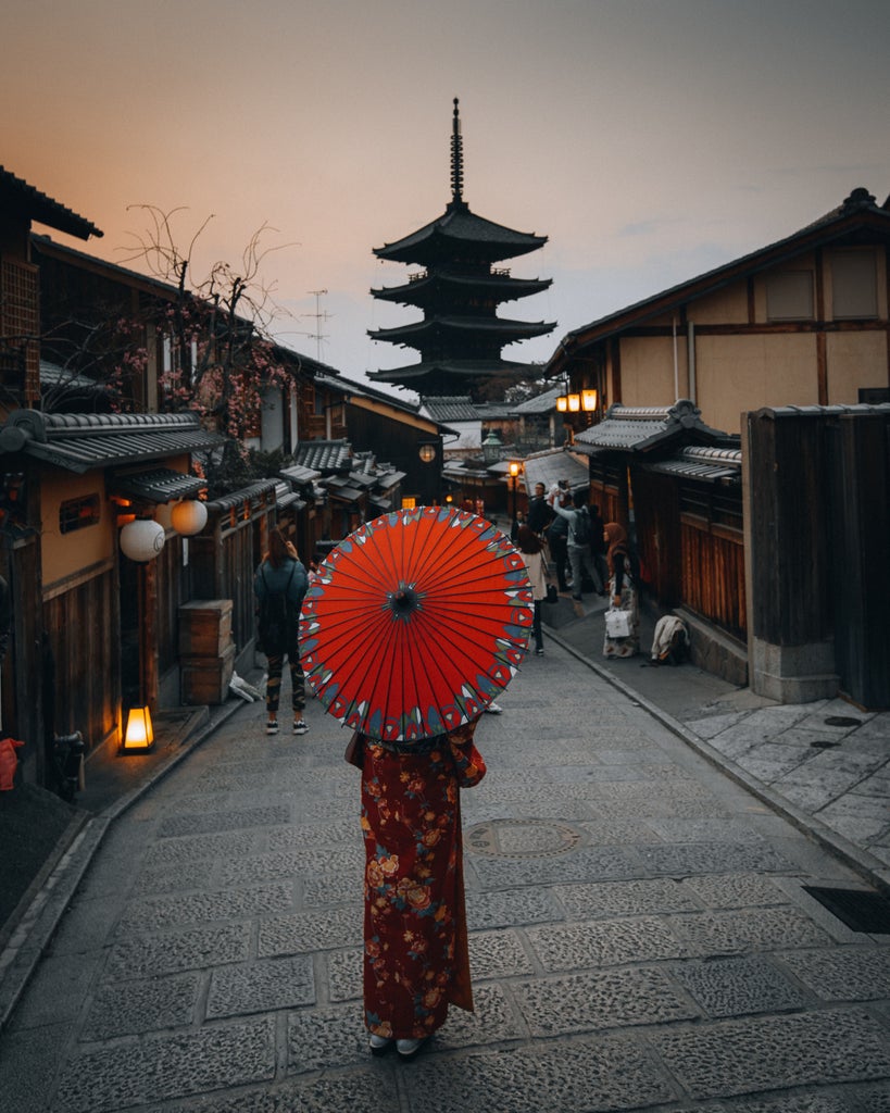 Snow-capped Mount Fuji towering over a serene lake at sunset, with cherry blossoms framing traditional wooden pagoda on water's edge