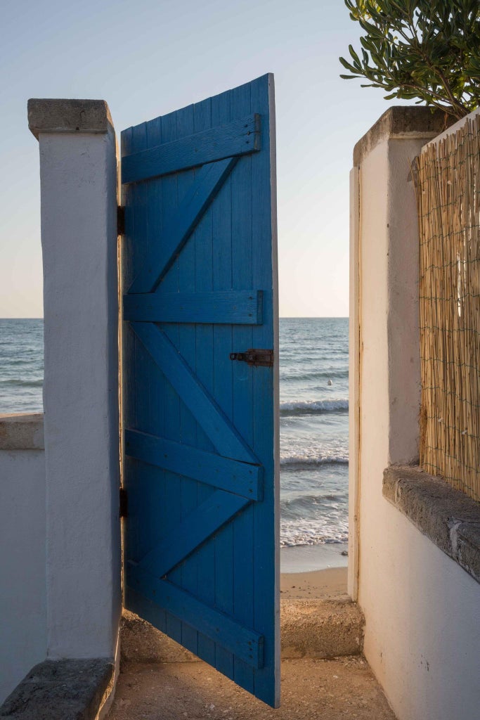 Elegant white-washed luxury hotel with Mediterranean architecture, featuring a pristine pool overlooking sun-drenched coastal landscape in southern Italy