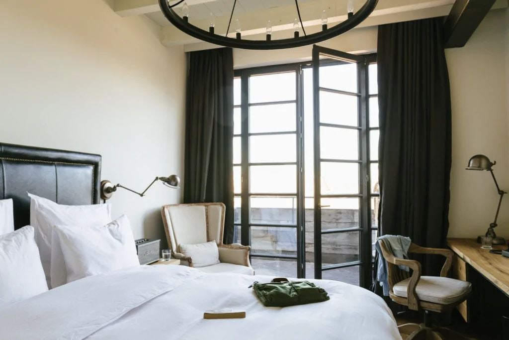 Luxurious Rooms Hotel Tbilisi terrace with plush queen bed, floor-to-ceiling windows overlooking city skyline, modern minimalist design with warm wood tones