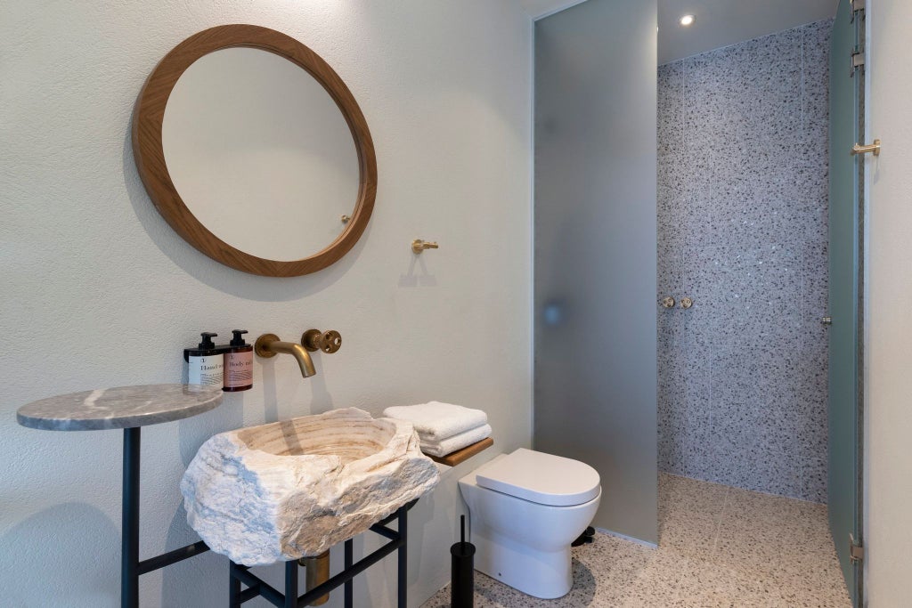 Minimalist luxury hotel room with neutral tones, wooden furniture, crisp white linens, and a glimpse of Athenian urban landscape through a modern window frame.