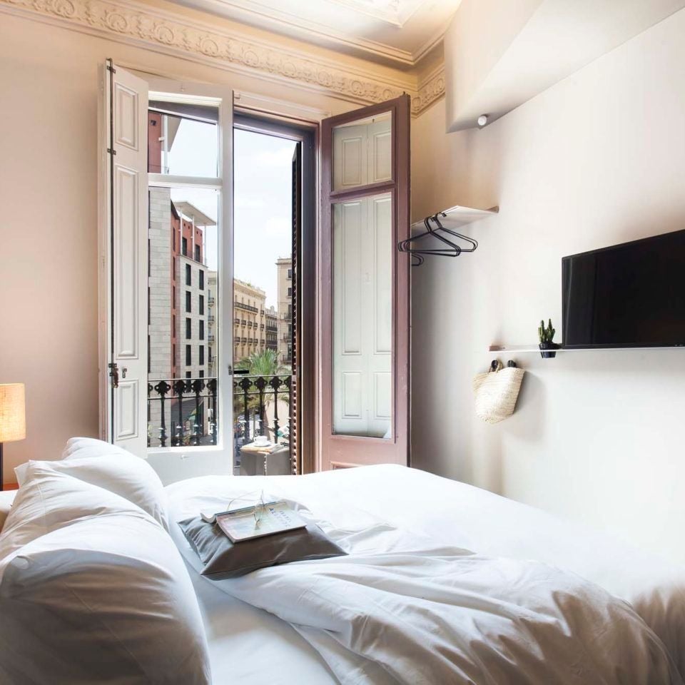 Elegant modern hotel room with minimalist design, crisp white linens, sleek wooden furniture, and panoramic city view of Barcelona's skyline