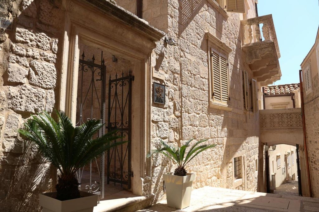 Historic stone palace hotel with rustic beige facade, arched windows, and ornate balconies set against a backdrop of blue Adriatic waters