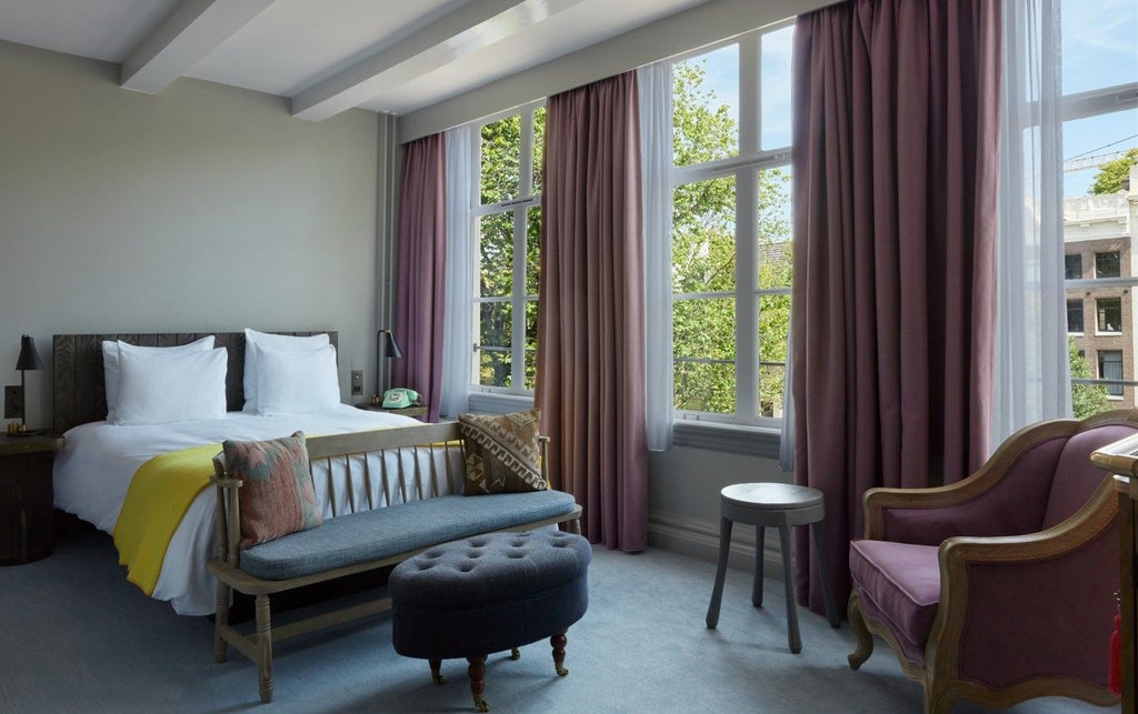 Elegant Amsterdam hotel room with canal views, featuring exposed wooden beams, plush bed with crisp linens, and refined vintage decor